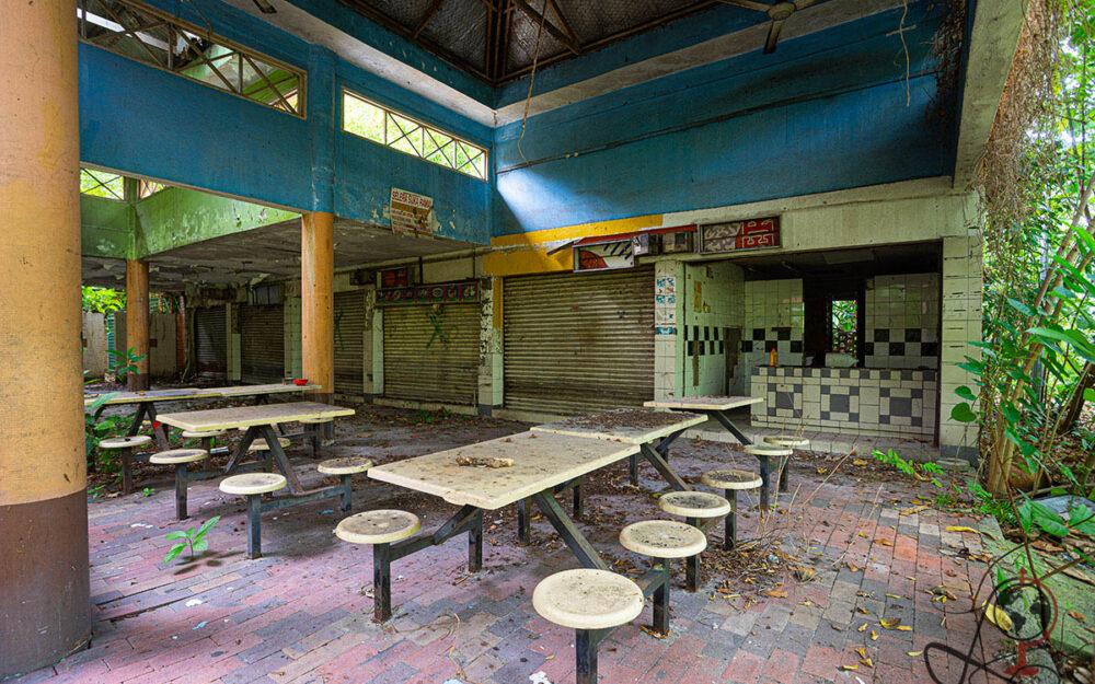 Großer Innenraum mit blauen Wänden, geschlossenen Ständen, Tischen und Laub auf Ziegelboden