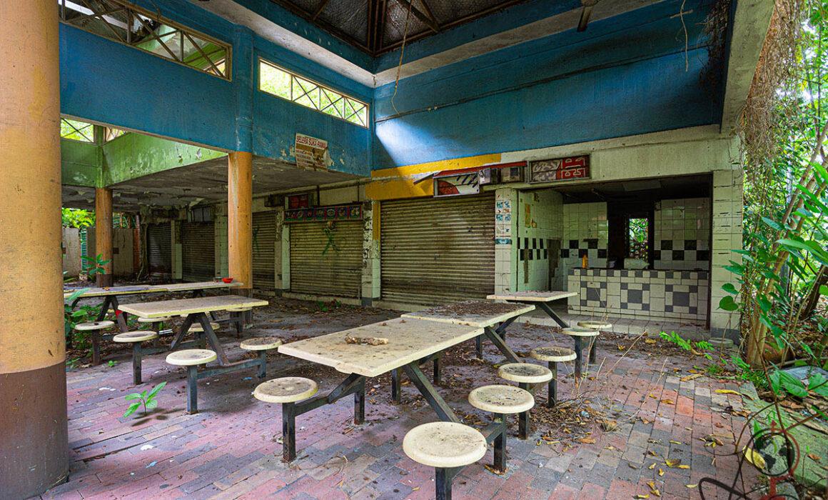 Großer Innenraum mit blauen Wänden, geschlossenen Ständen, Tischen und Laub auf Ziegelboden