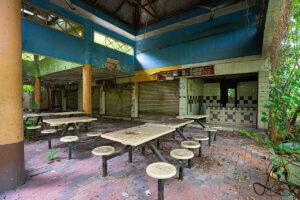 Großer Innenraum mit blauen Wänden, geschlossenen Ständen, Tischen und Laub auf Ziegelboden