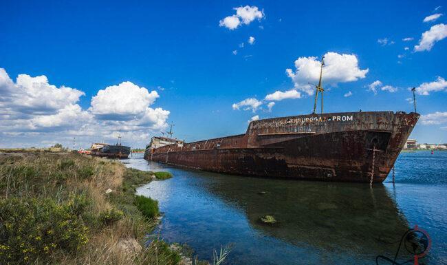Verlassenes rostiges Frachtschiff am Ufer eines Hafenbeckens unter blauem Himmel mit weißen Wolken