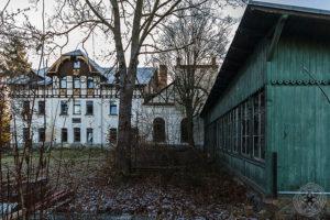 Verlassenes Waldhaus Mehltheuer mit weiß verputztem Fachwerkgiebel und grünem Holzanbau im verwilderten Hof.