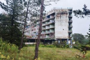 Hotel Aia in Tskaltubo: verwitterte Fassade des ehemaligen Kurhotels zwischen Bäumen und hohem Gras.
