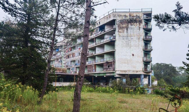 Hotel Aia in Tskaltubo: verwitterte Fassade des ehemaligen Kurhotels zwischen Bäumen und hohem Gras.
