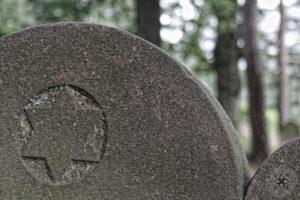 Detail eines abgerundeten Grabsteins mit einem verblassten eingemeißelten Symbol