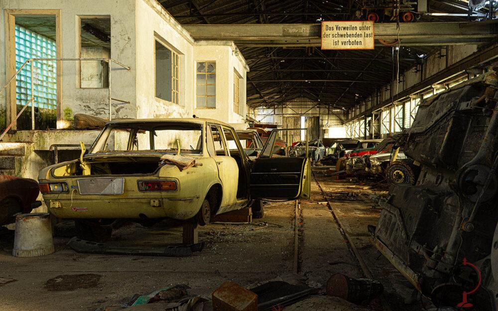 Verlassene Autos vor Bürohaus in der Werkhalle, Warnschild hängt über den Schienen