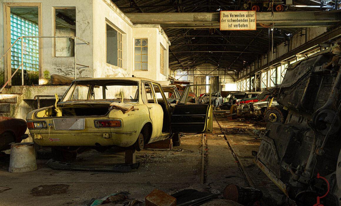 Verlassene Autos vor Bürohaus in der Werkhalle, Warnschild hängt über den Schienen