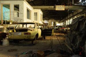 Verlassene Autos vor Bürohaus in der Werkhalle, Warnschild hängt über den Schienen