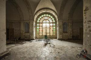 Verlassener Saal im ehemaligen Manicomio di Colorno mit großem farbigem Rundfenster und abblätterndem Wandputz.