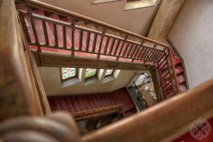 Historisches Treppenhaus mit rotem Handlauf, Holzgeländer und beschädigter Decke
