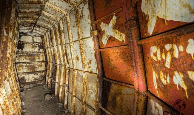 Innenansicht des Bunkers mit rostiger Tür und abgeblätterter roter Wandfarbe