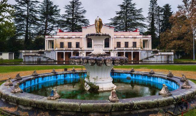 Brunnen mit einer Skulptur vor der symmetrischen Fassade des ehemaligen Bahnhofs Tskaltubo in Georgien.