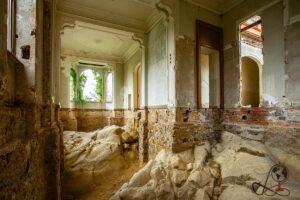 Verfallener Innenraum der Villa Pallavicino Gardino mit freiliegendem Felsgestein, beschädigten Wänden und Rundbogenfenstern