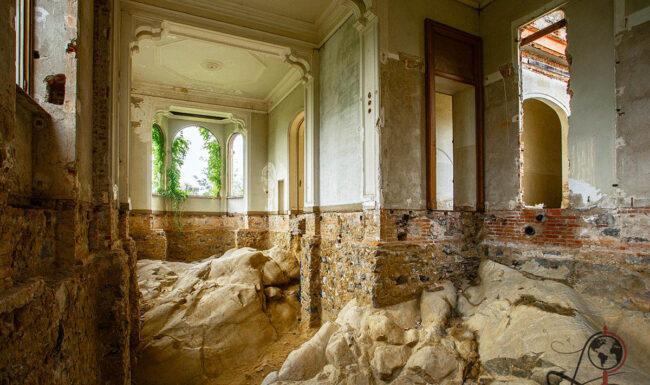 Verfallener Innenraum der Villa Pallavicino Gardino mit freiliegendem Felsgestein, beschädigten Wänden und Rundbogenfenstern